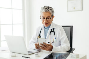 Female physician on her phone and laptop reading and replying to patient reviews