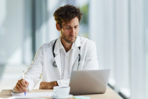 Young male medical expert writing down his plans while working on a computer in the office