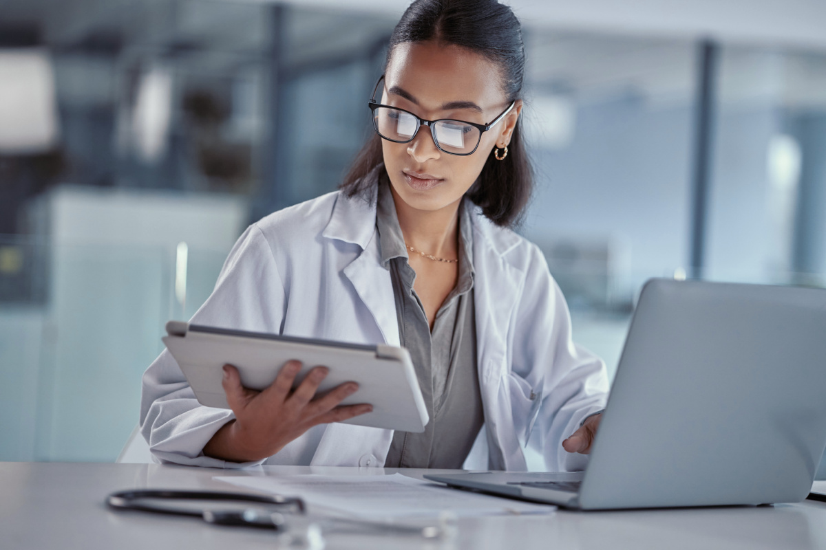 Female physician looking at patient information on laptop and tablet