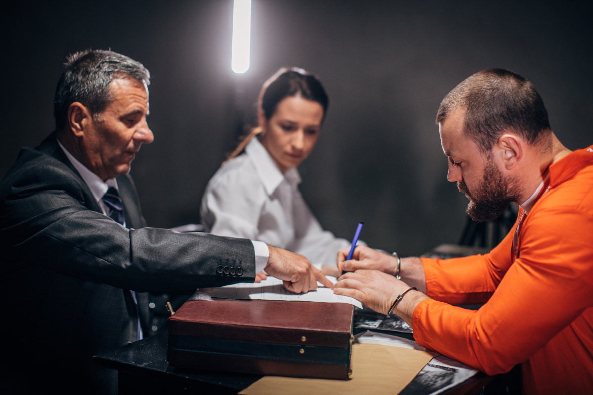 Male prisoner in orange jumpsuit reviewing healthcare paperwork with lawyers