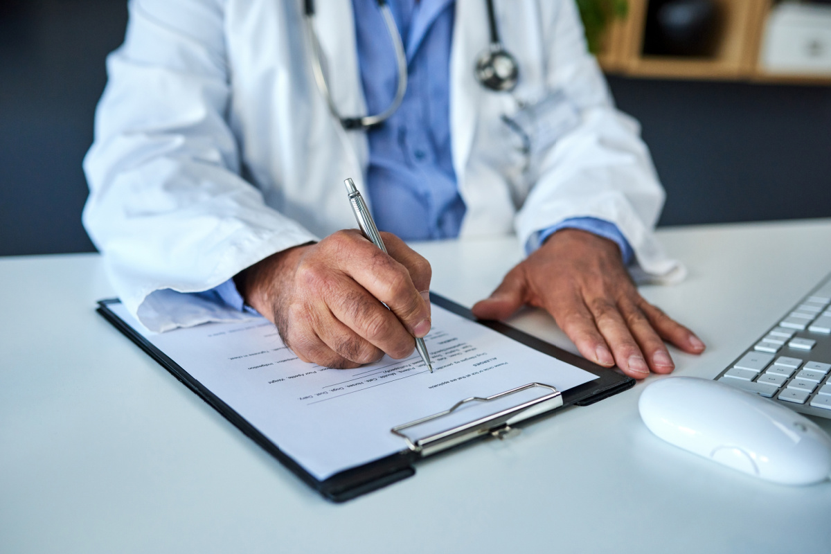 Faceless male physician in white doctor's coat filling out medical license renewal application
