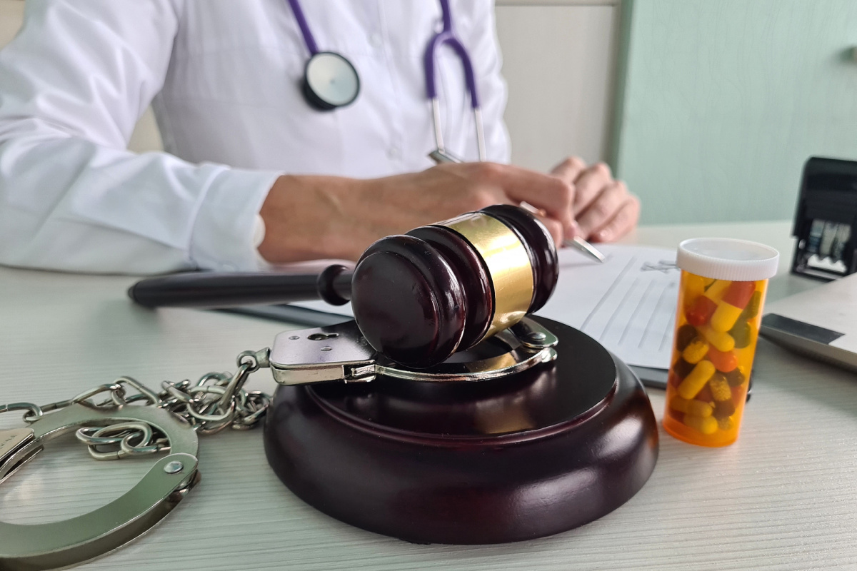 Gavel on paper while physician signs paperwork with pills and handcuffs