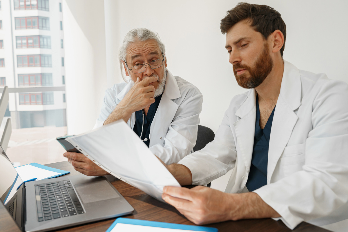 Two male physicians business partners with medical practice frowning at legal documents